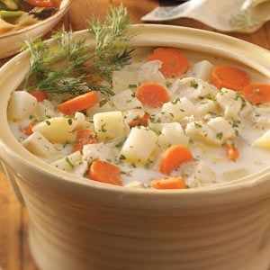 a bowl of soup with carrots, potatoes and dill on the side sitting on a table