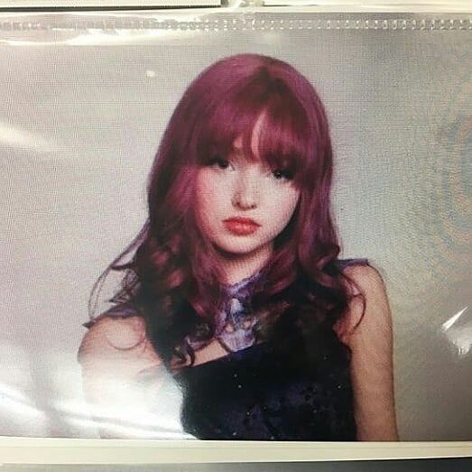 a young woman with red hair and bangs posing for a photo in front of a white wall