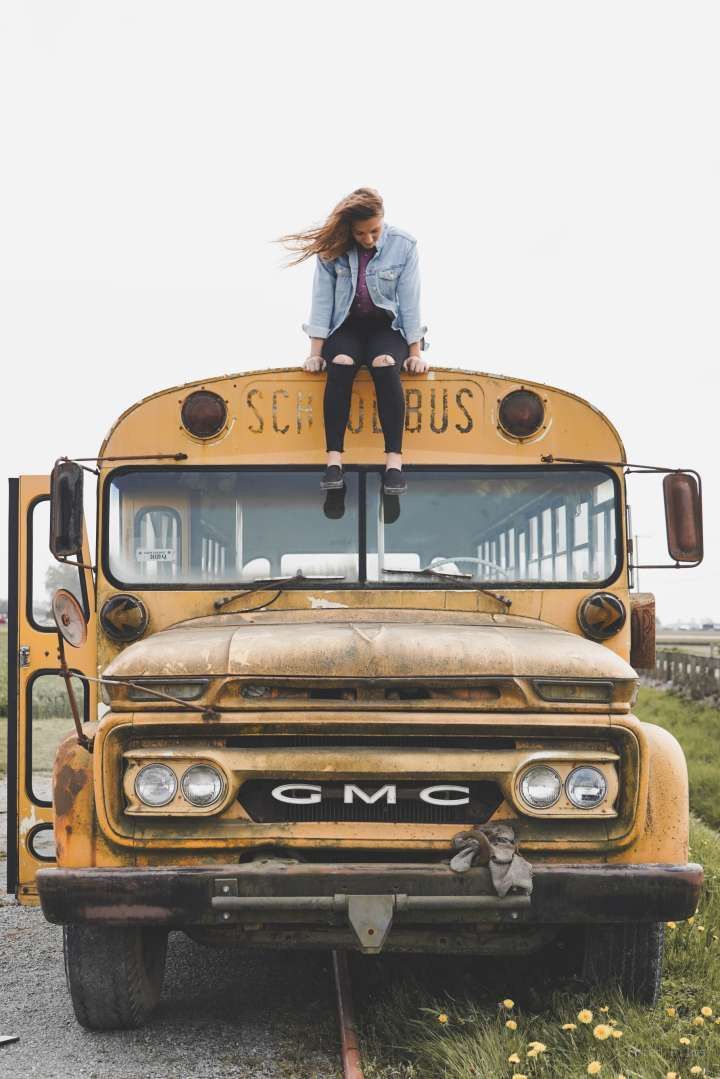 a woman sitting on top of an old yellow school bus in the middle of nowhere