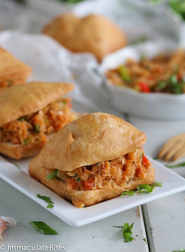 two sandwiches on a white plate with silverware in the background and another bowl of food to the side