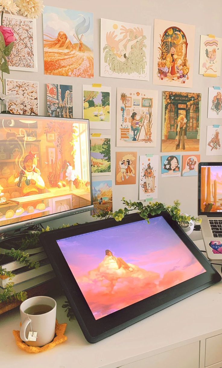 there are two computers on the desk with pictures on the wall behind them and a coffee cup in front of it