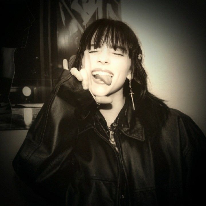 a woman with black hair and piercings making a funny face while wearing a leather jacket