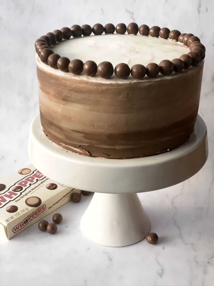 a chocolate cake with white frosting on a stand next to a box of candy