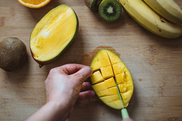 a person cutting up some fruit on a wooden table with kiwis and oranges