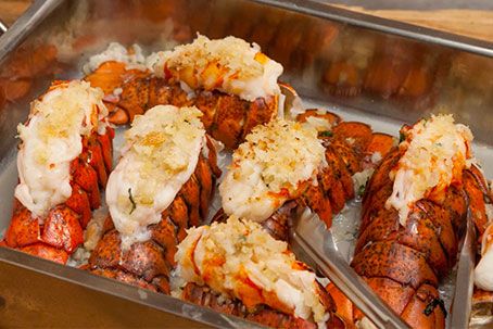 cooked lobsters and other seafood are being served in a large metal pan with tongs