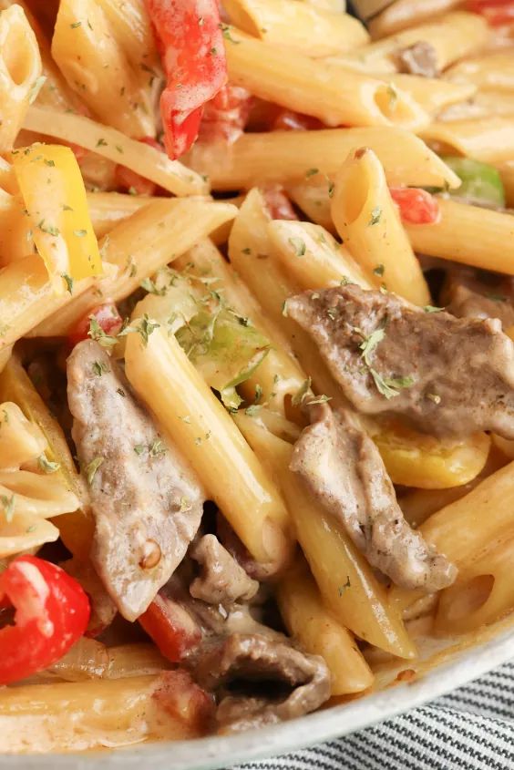 pasta with meat and vegetables in a white bowl on a table cloth, ready to be eaten