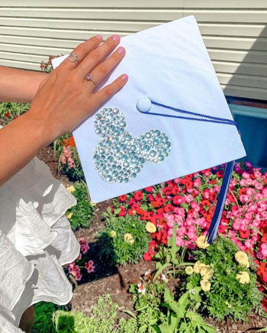 a woman holding up a card with a mickey mouse on it in front of flowers