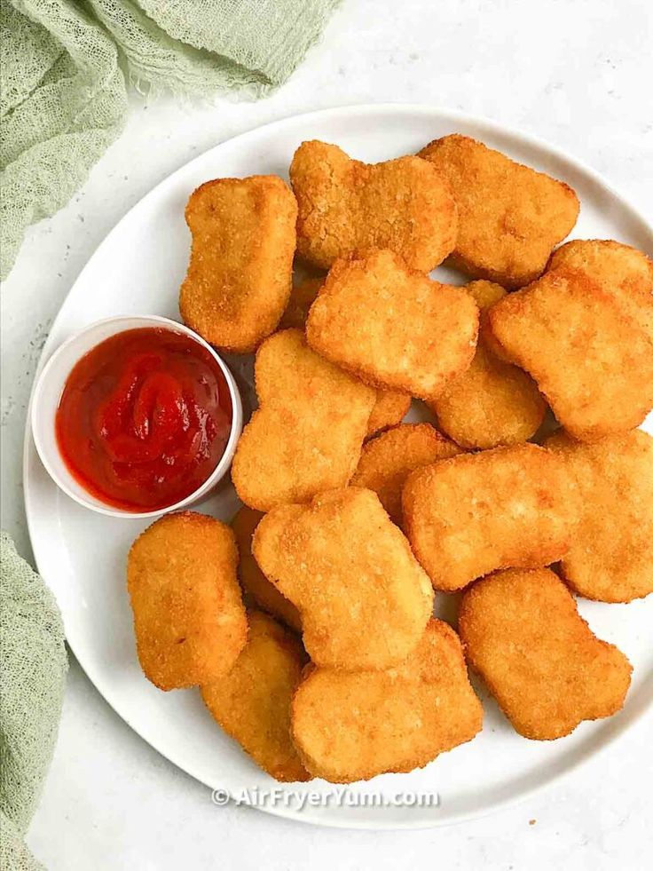 some fried food on a white plate with ketchup and dipping sauce in the middle