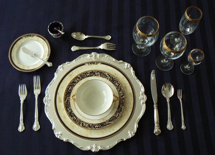 the table is set with silver and gold dishes, forks, spoons, cups, and knives