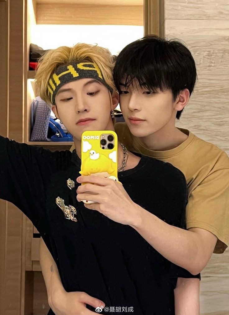 two young men taking a selfie in front of a mirror with their cell phones