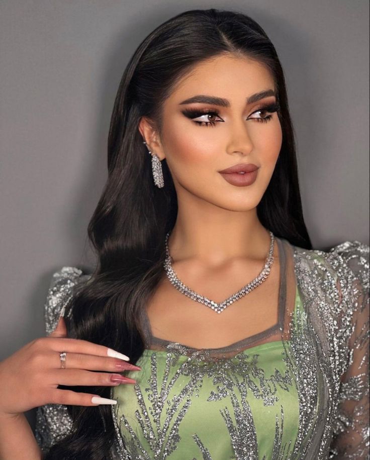 a woman with long dark hair wearing a green dress and diamond jewelry, posing for the camera