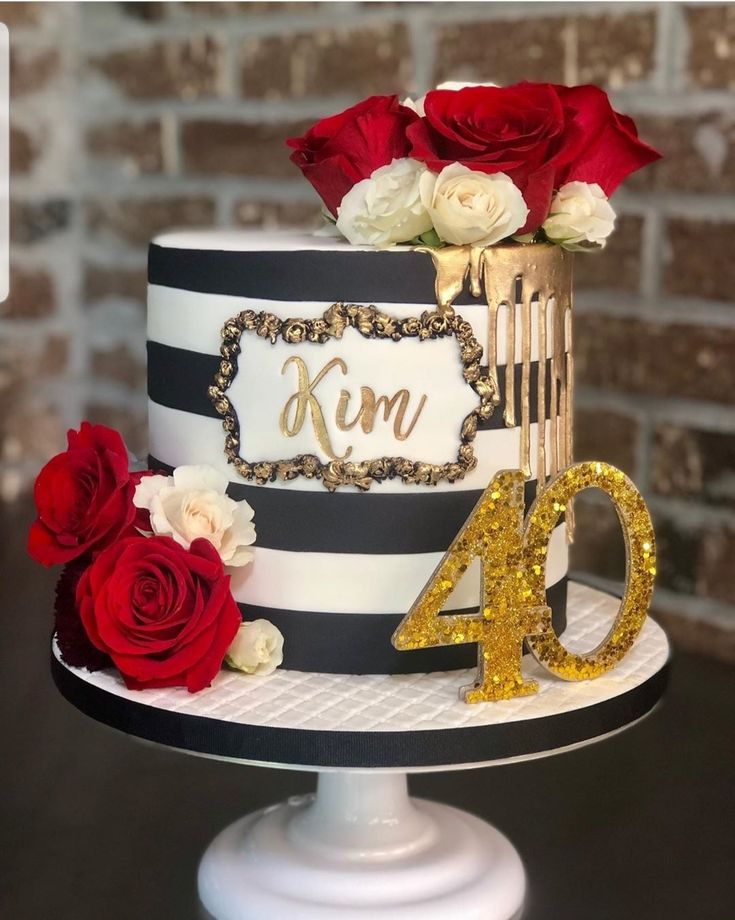 a black and white cake with red roses on the top is decorated with gold lettering