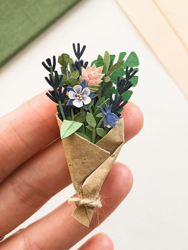 a hand holding a small bouquet of flowers on top of a piece of brown paper