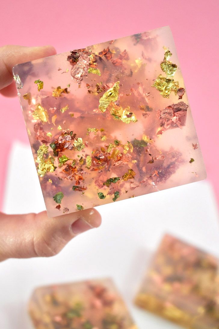 a hand holding up a square piece of pink and gold confetti with leaves on it