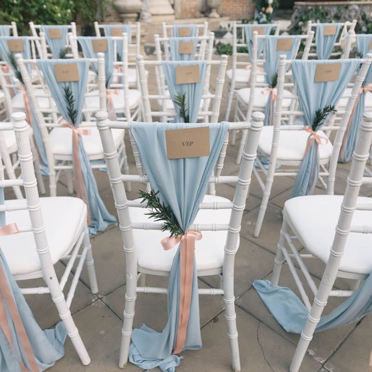 rows of white folding chairs with blue sashes and peach ribbons tied to them, decorated with greenery