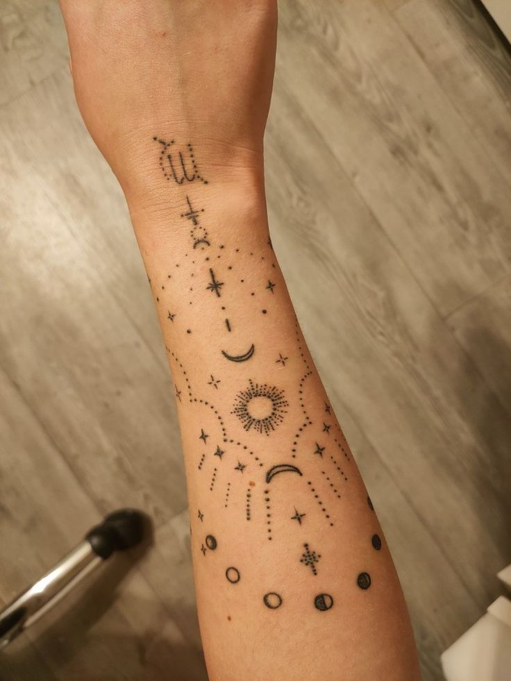 a woman's arm with stars and moon tattoos on her left wrist, while the other hand is holding a cell phone