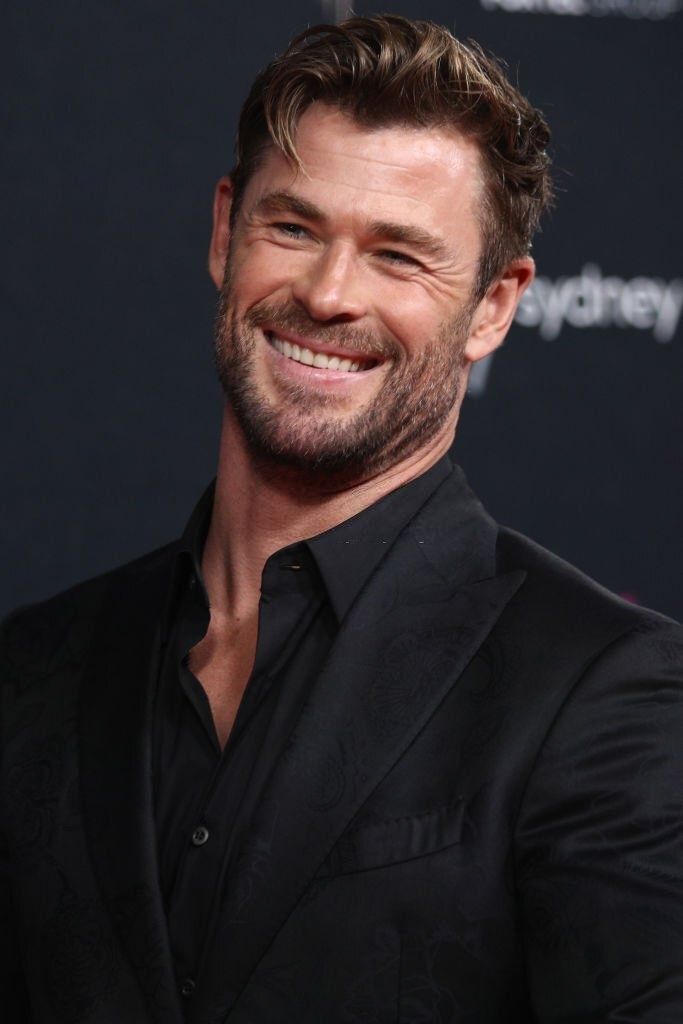 the actor is smiling and wearing a black suit