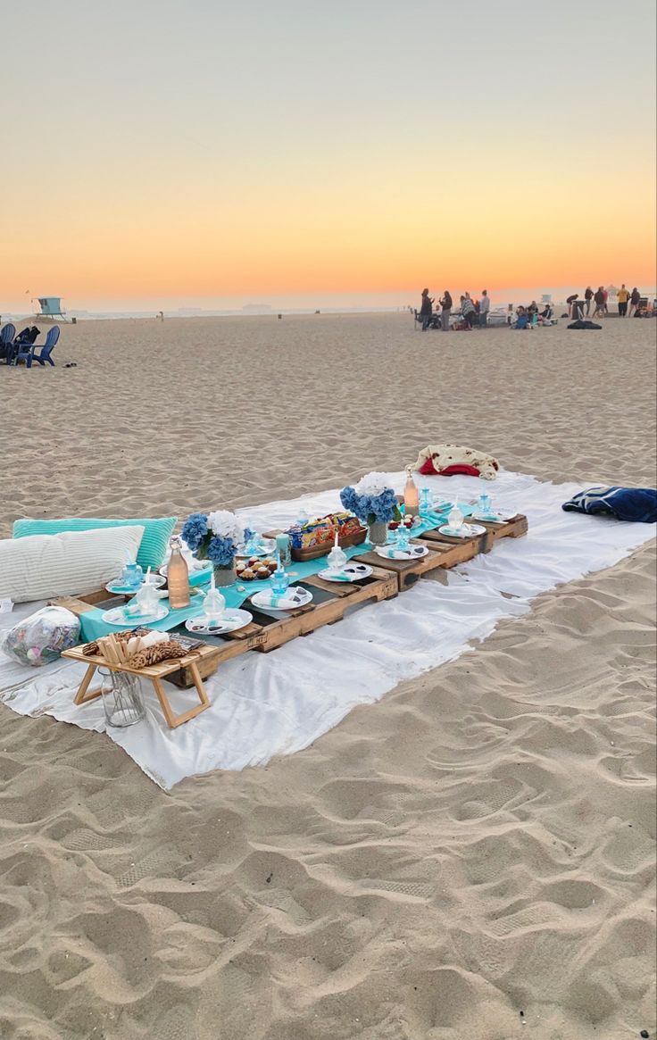 a long table set up on the beach for an outdoor dinner party with blue plates and napkins