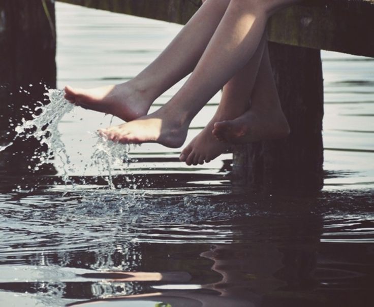 two people are sitting on a dock with their feet in the water and splashing