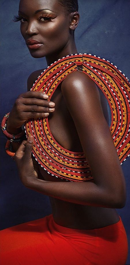 an african woman in a red skirt and headdress poses for the camera with her hands on her chest