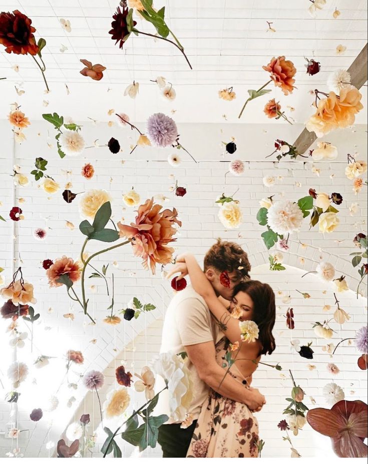 a man and woman standing in front of a wall with flowers hanging from the ceiling