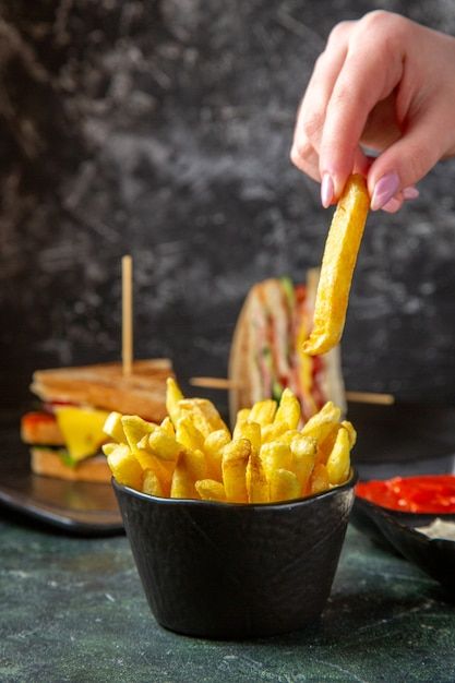 a person is dipping french fries into a black bowl on a table with other food