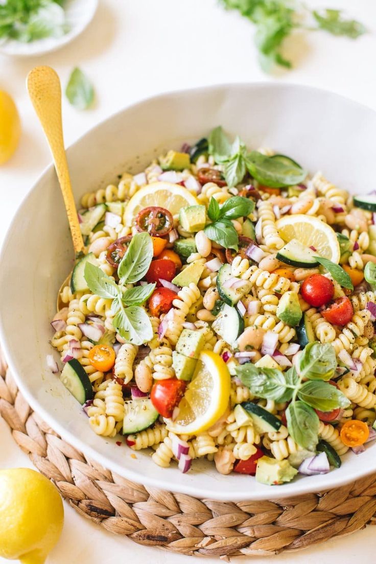 a white bowl filled with pasta salad next to sliced lemons and basil on the side