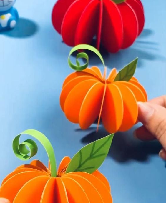 someone is cutting out paper pumpkins on a blue surface with other decorations behind them