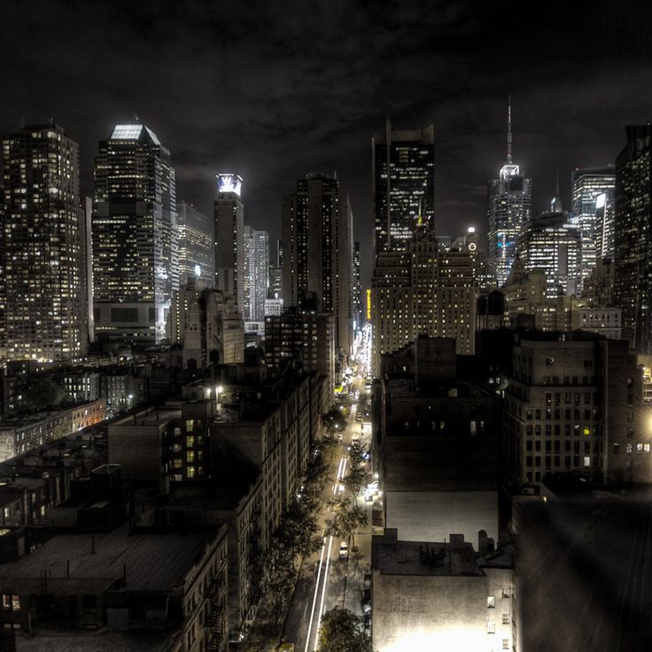 the city skyline is lit up at night with skyscrapers in the foreground and dark clouds overhead