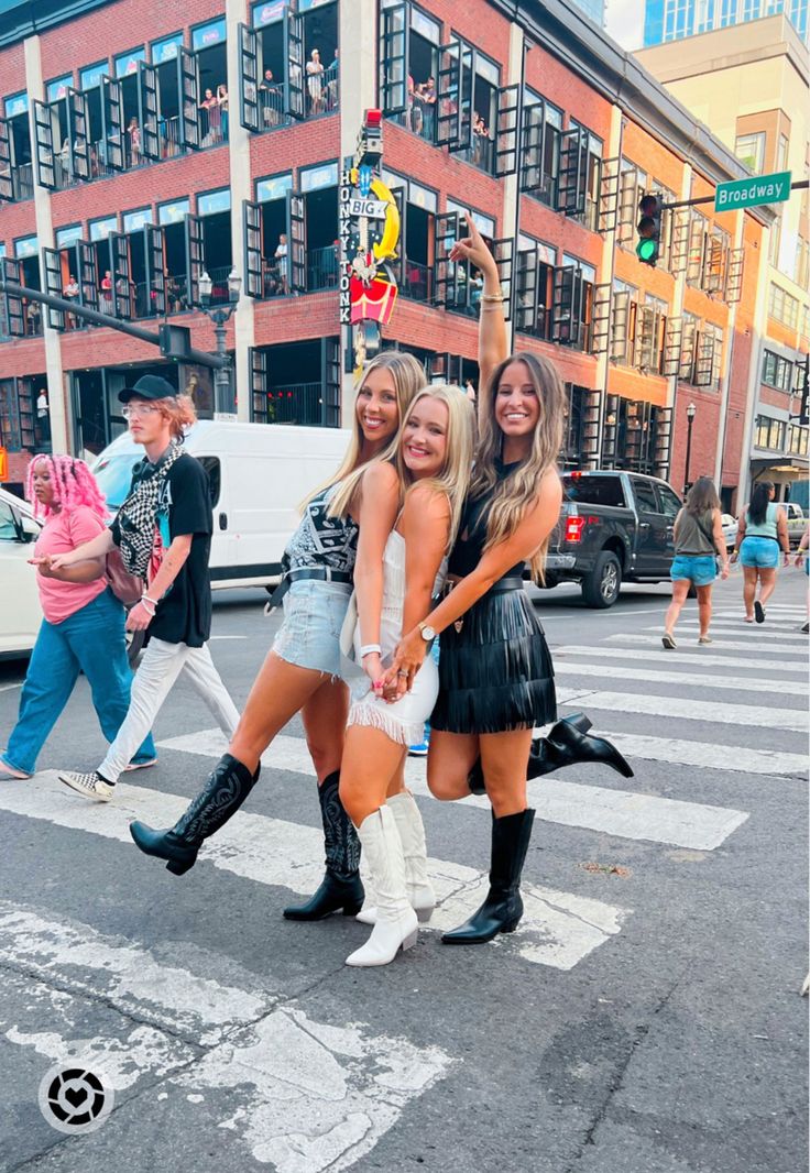 three women in short skirts and boots are posing for the camera while crossing the street