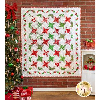 a christmas quilt hanging on a brick wall next to a small tree with red and green ornaments