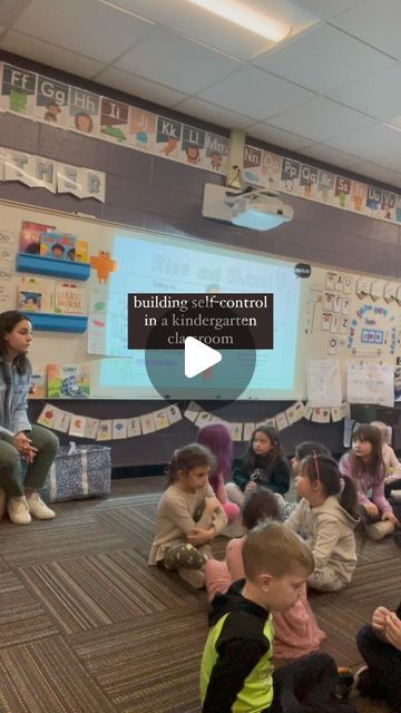 a group of children sitting on the floor in front of a projector screen with words above them