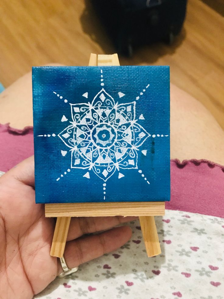 a hand holding a small blue and white painting on an easel