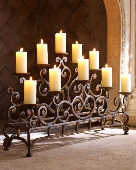 a large metal candle holder with many lit candles on it's sides, in front of a fireplace