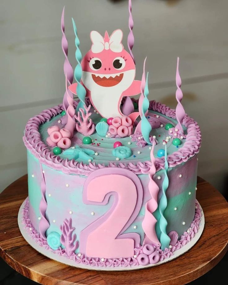 a pink and blue birthday cake with a shark on it's face, under the seaweed