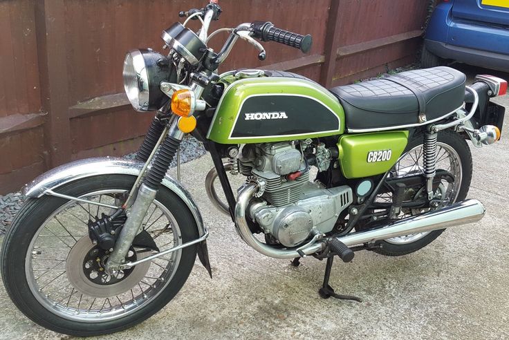 a green and black motorcycle parked in front of a wooden fence next to a blue car