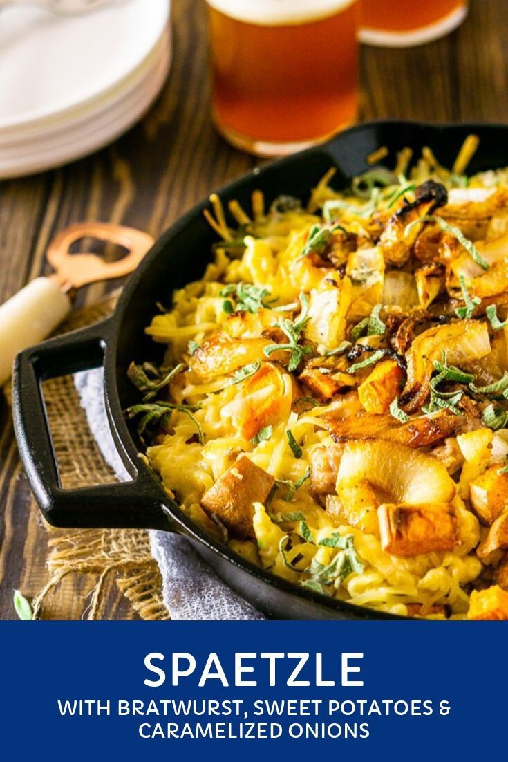 a skillet filled with pasta and vegetables on top of a wooden table next to beer glasses