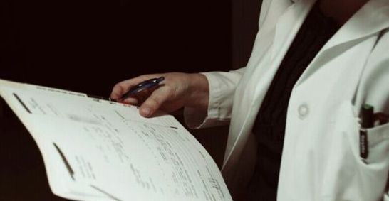 a person in a white lab coat holding a pen and paper with writing on it