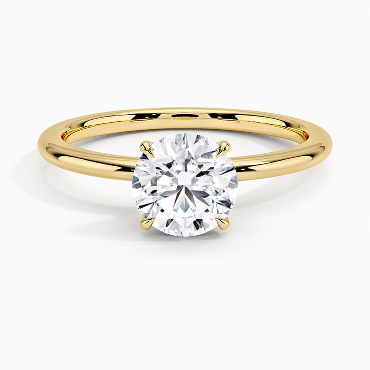 a yellow gold engagement ring with a round cut diamond in the center, on a white background