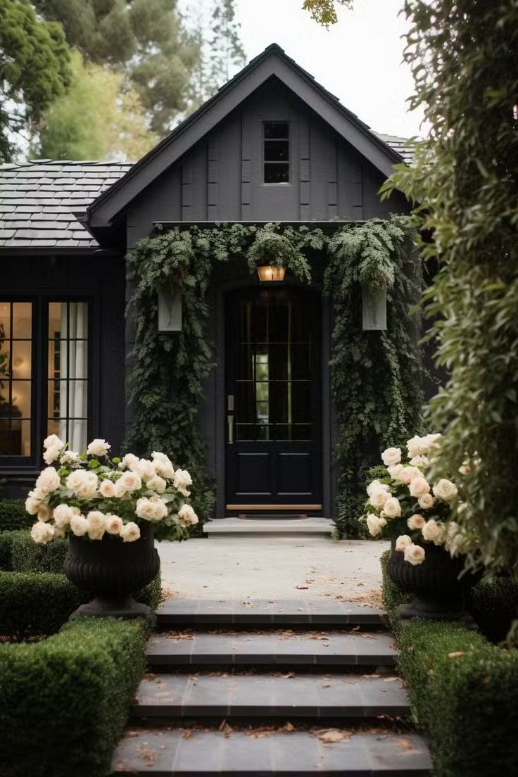 a black house with white flowers in the front yard and steps leading up to it