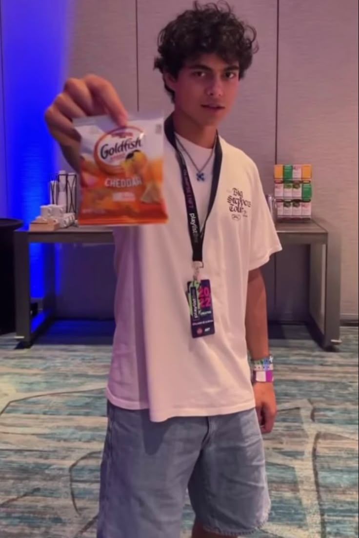 a young man is holding up a box of chips in front of the camera while standing on a carpeted floor