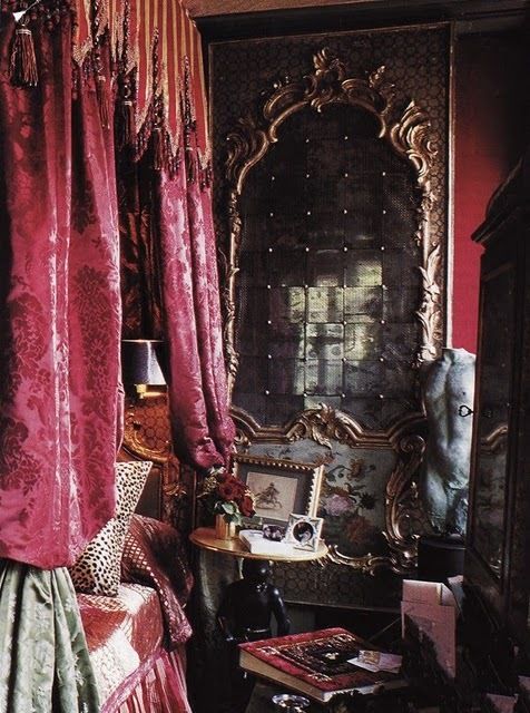 a bedroom with red curtains and an ornate mirror in the corner next to a bed