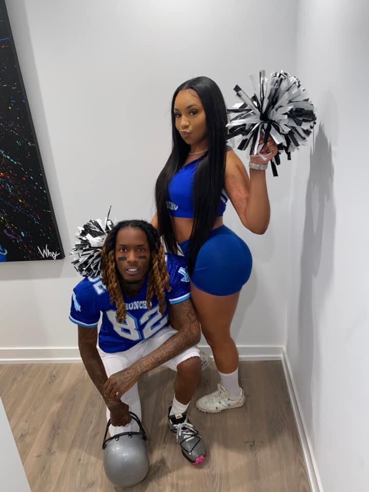 two cheerleaders pose for a photo in front of a wall with a painting