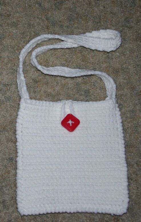 a white crocheted bag with a red button on it sitting on the floor