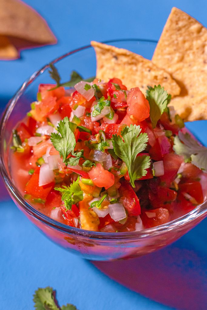 a glass bowl filled with salsa and tortilla chips on top of a blue surface