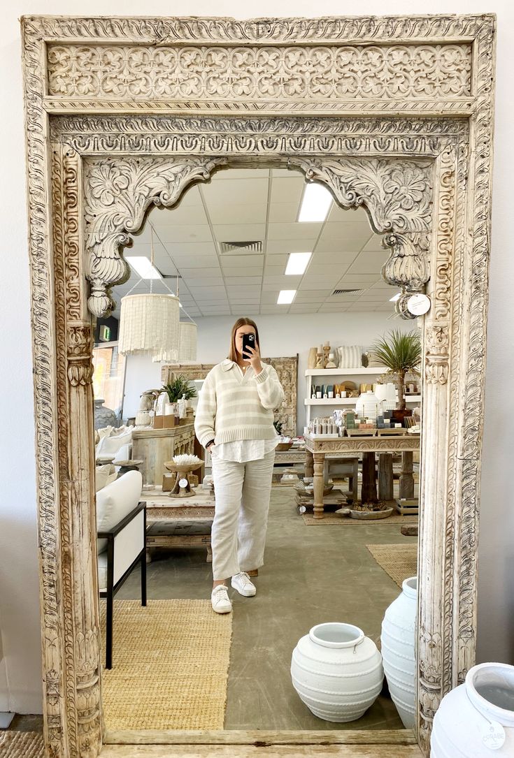 a woman taking a selfie in front of a mirror with vases on the floor