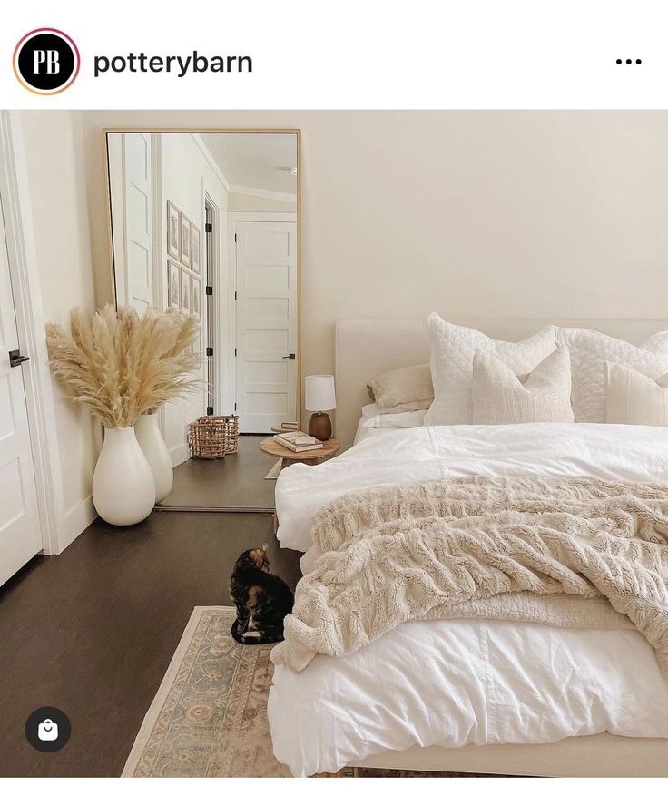 a cat laying on the floor in front of a bed with white sheets and pillows