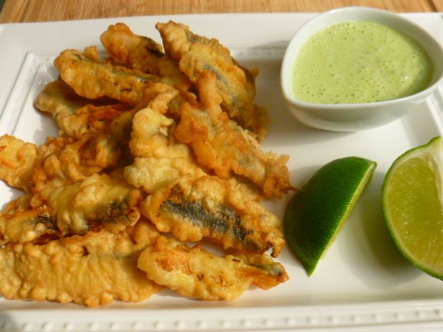 a white plate topped with fried food next to a bowl of green liquid and a lime