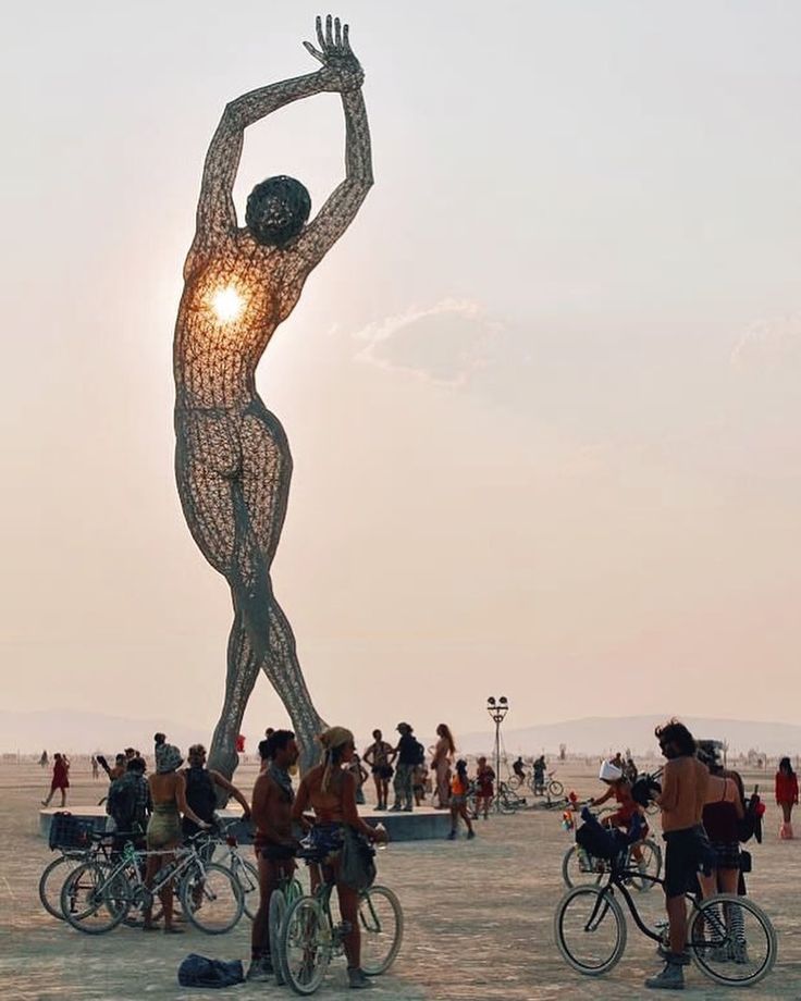 the sun is setting behind a large statue in the middle of a beach with many people on bikes