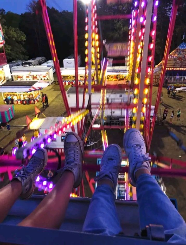 two people sitting on a carnival ride with their feet up in the air at night